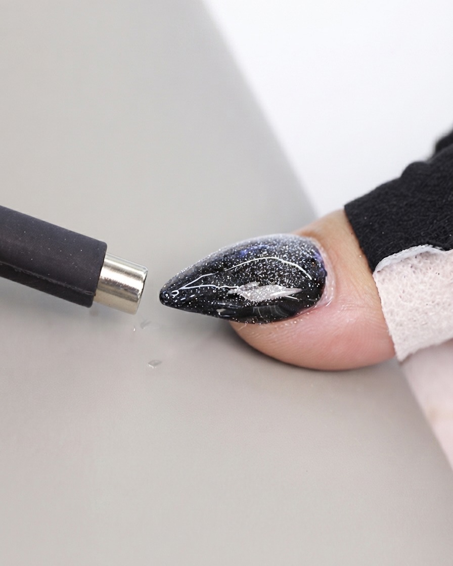 A black pen-style magnet tool being brought close to a textured cat eye nail surface.