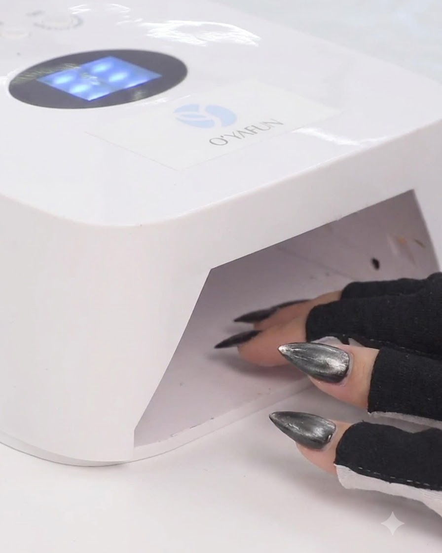 A hand in black fingerless gloves placing fingers inside a white UV LED nail lamp to cure gel polish.