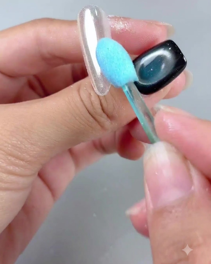A blue-handled brush gently sweeping away powder from a glossy mirror-finished nail tip.