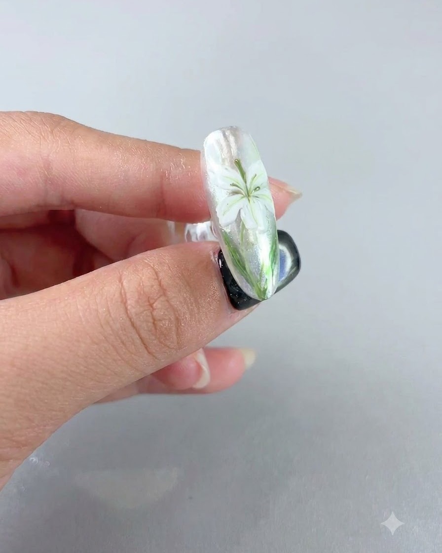 A completed nail showing a white lily design under a velvet matte sealing coat.