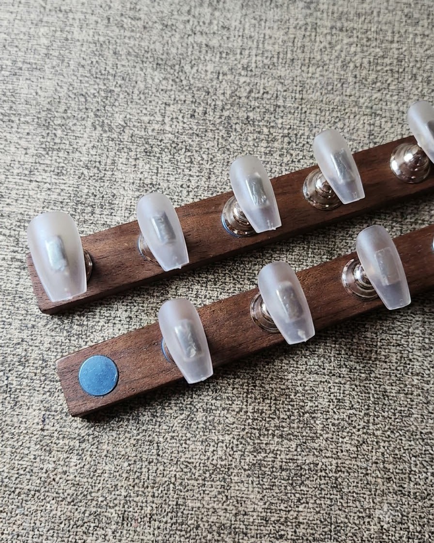 A lint-free wipe cleaning dust off prepped clear nail tips arranged on a wooden stand.