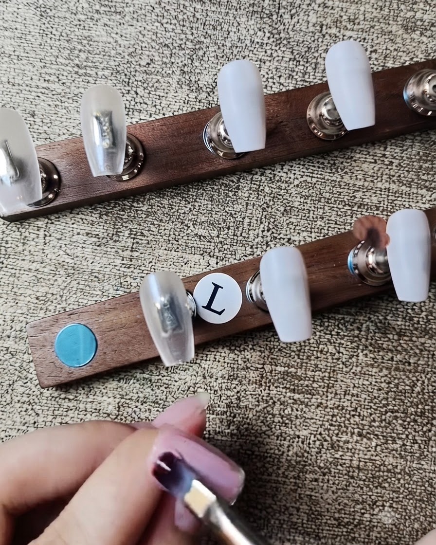 A flat gel brush applying sheer nude pink gel polish onto a press-on nail.