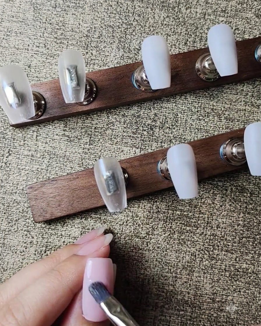 A flat gel brush applying a second layer of sheer nude pink gel polish to the nail.