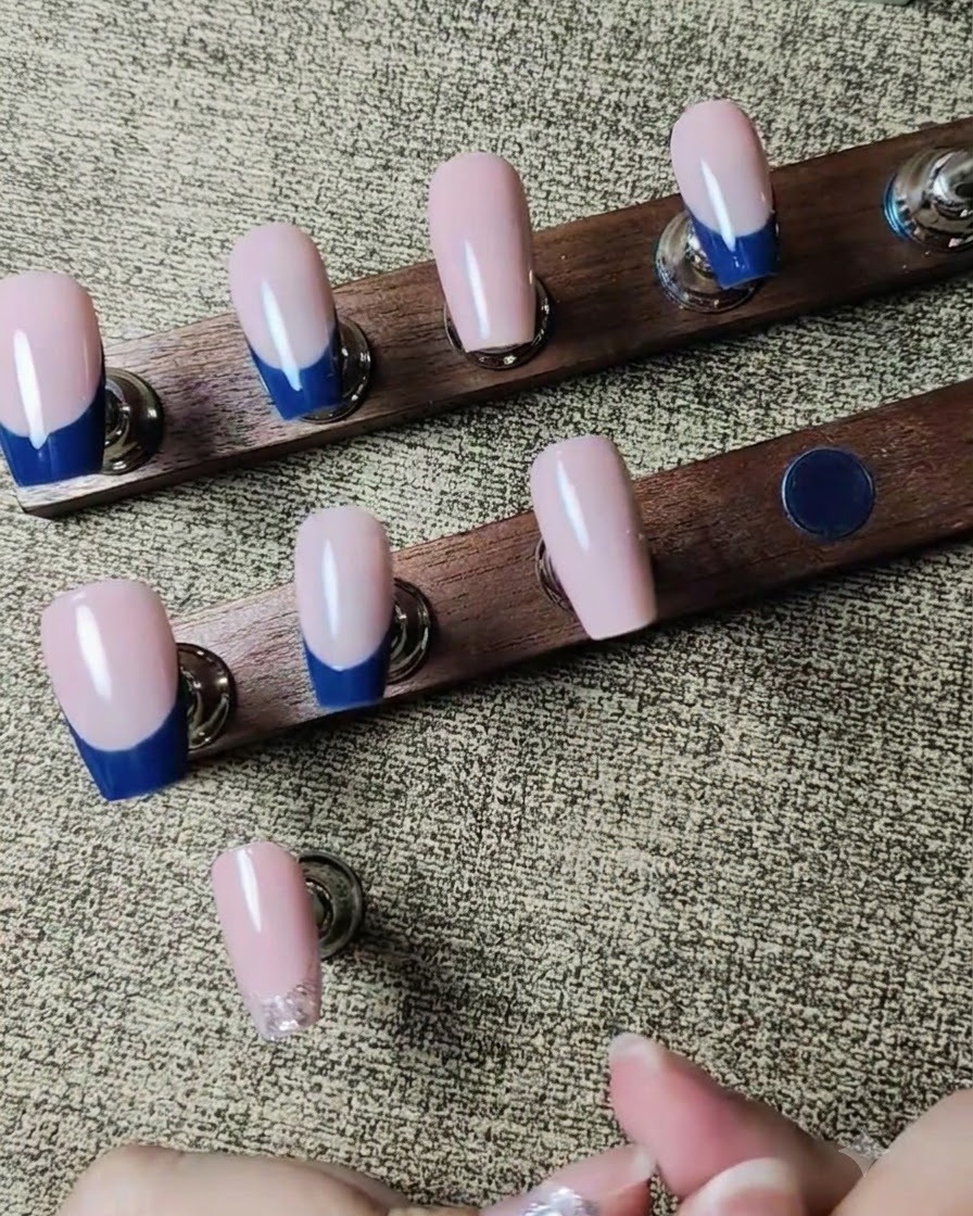 A tool placing tiny clear rhinestones onto a wet silver glitter line on a nail.