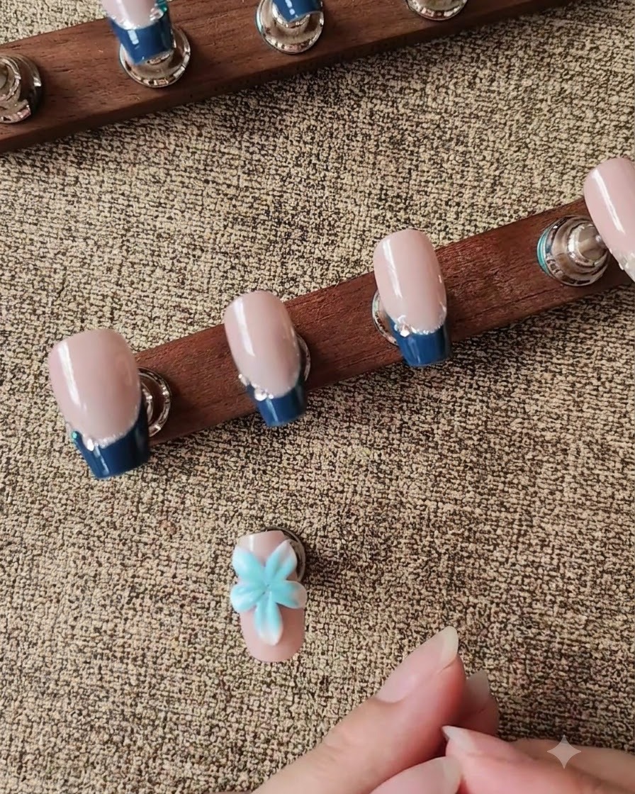 A silicone carving tool shaping a 3D white flower petal on a press-on nail.