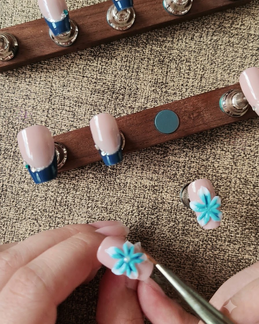 A wax pen placing a white pearl into the center of a blue and white 3D nail flower.