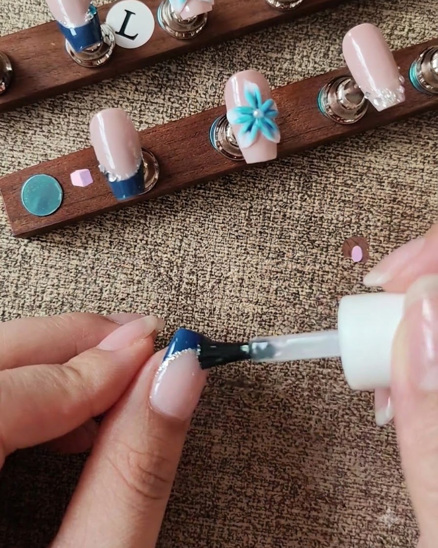 A brush applying top coat onto the nail surface while navigating around a 3D floral accent.