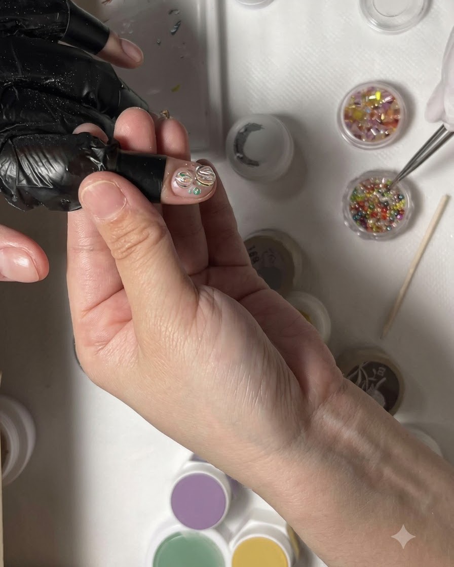 A pair of tweezers placing a cluster of tiny colorful rhinestones into the center of a nail design.