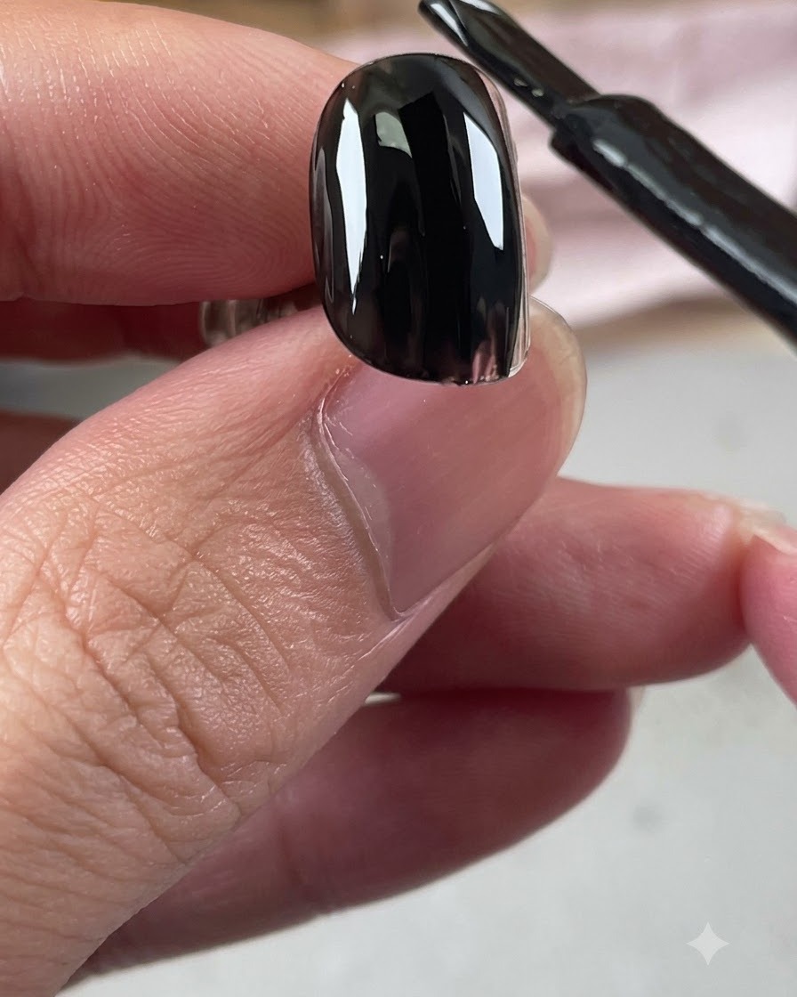 A black gel polish bottle brush applying a glossy layer of black base coat onto a nail.