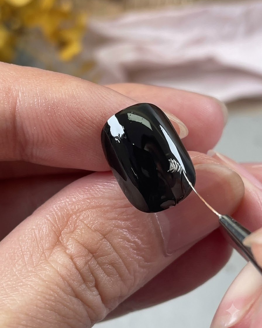 A close-up view of a hand using a fine nail art brush to draw silver petal outlines on a black nail.