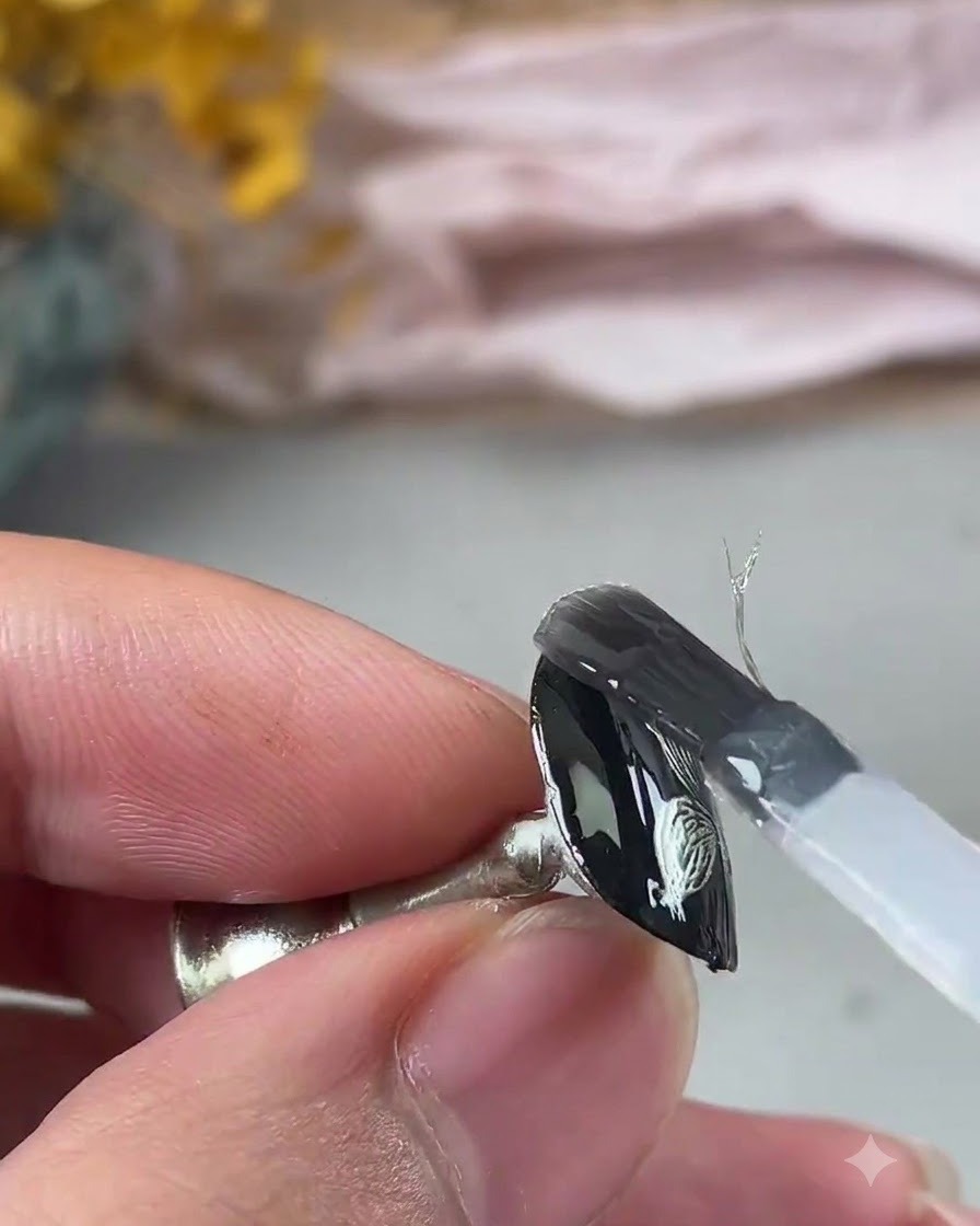 A brush applying a clear reinforcing gel coat over the textured metallic nail art design.