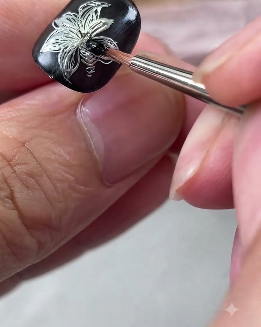 A detail brush blending black gel polish at the center of a silver metallic lily nail art design.