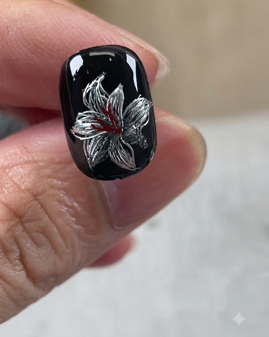 A completed metallic lily nail art design featuring a black base, silver petals, white accents, and red center details.