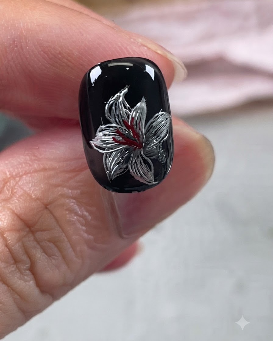 A completed metallic lily nail art design on a black base with red and silver details under a glossy top coat.