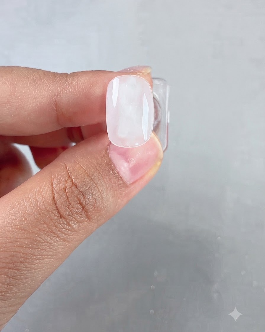 A close-up of a brush applying a clear, glossy gel layer onto a milky white base nail.