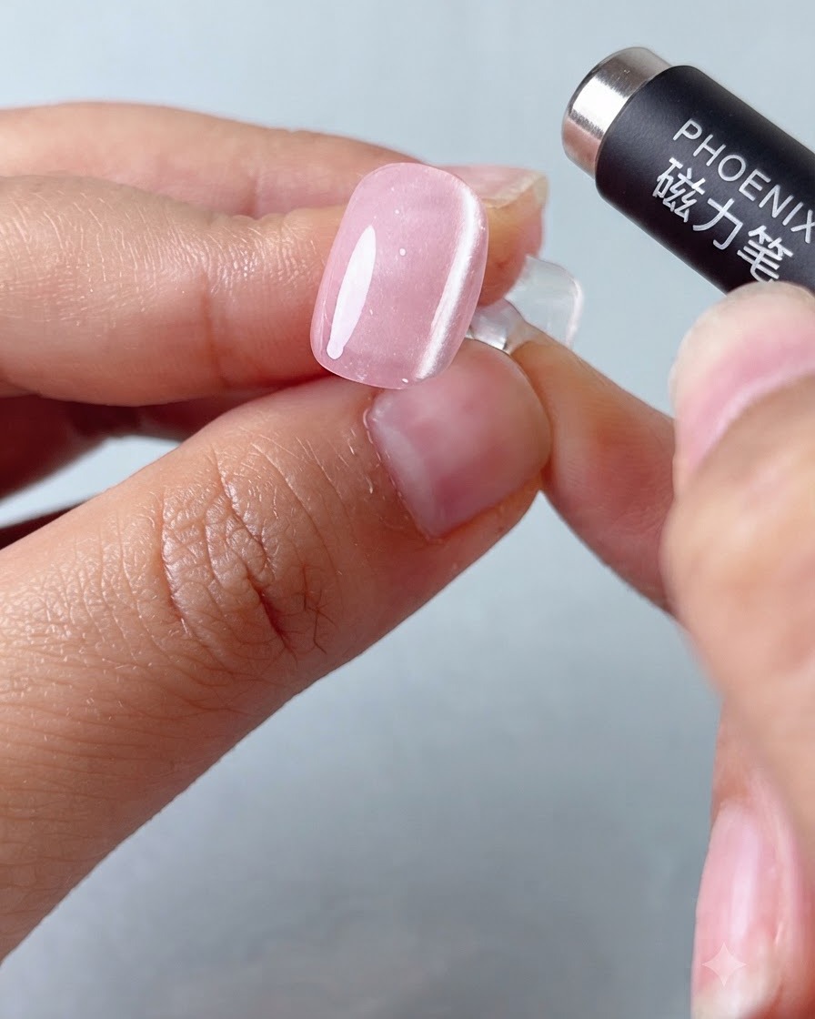 A magnetic pen tool hovering over a pink cat-eye gel nail to shape the light band.
