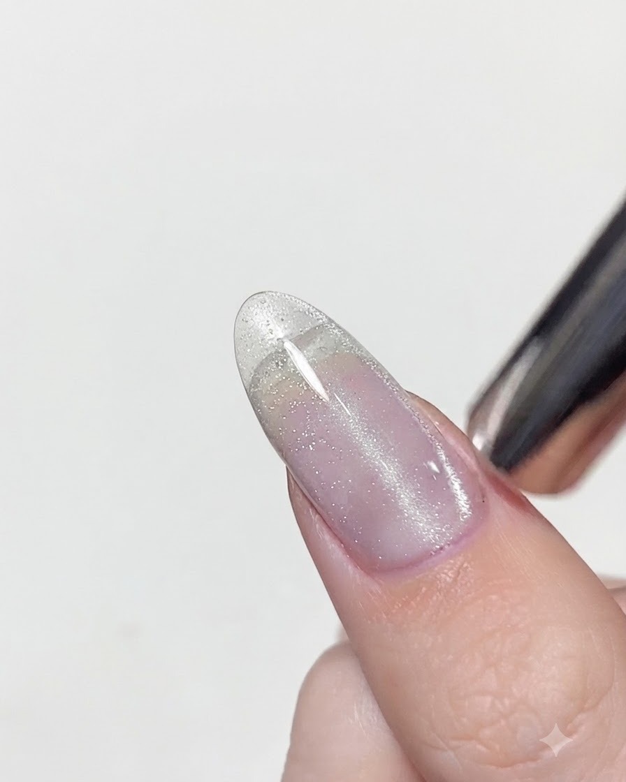 A magnetic tool positioned closely over a wet cat eye gel polished nail to concentrate the silver shimmer into a vertical line.