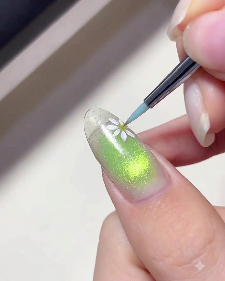 A fine liner brush applying white gel to paint delicate daisy petals on a green gradient nail.