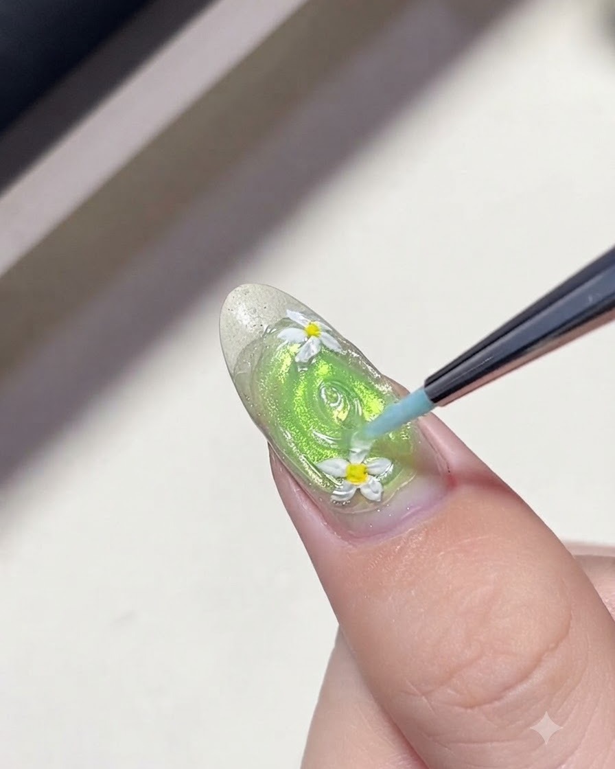 A fine liner brush drawing concentric rings of clear gel around daisy flowers on a green nail to create water ripples.