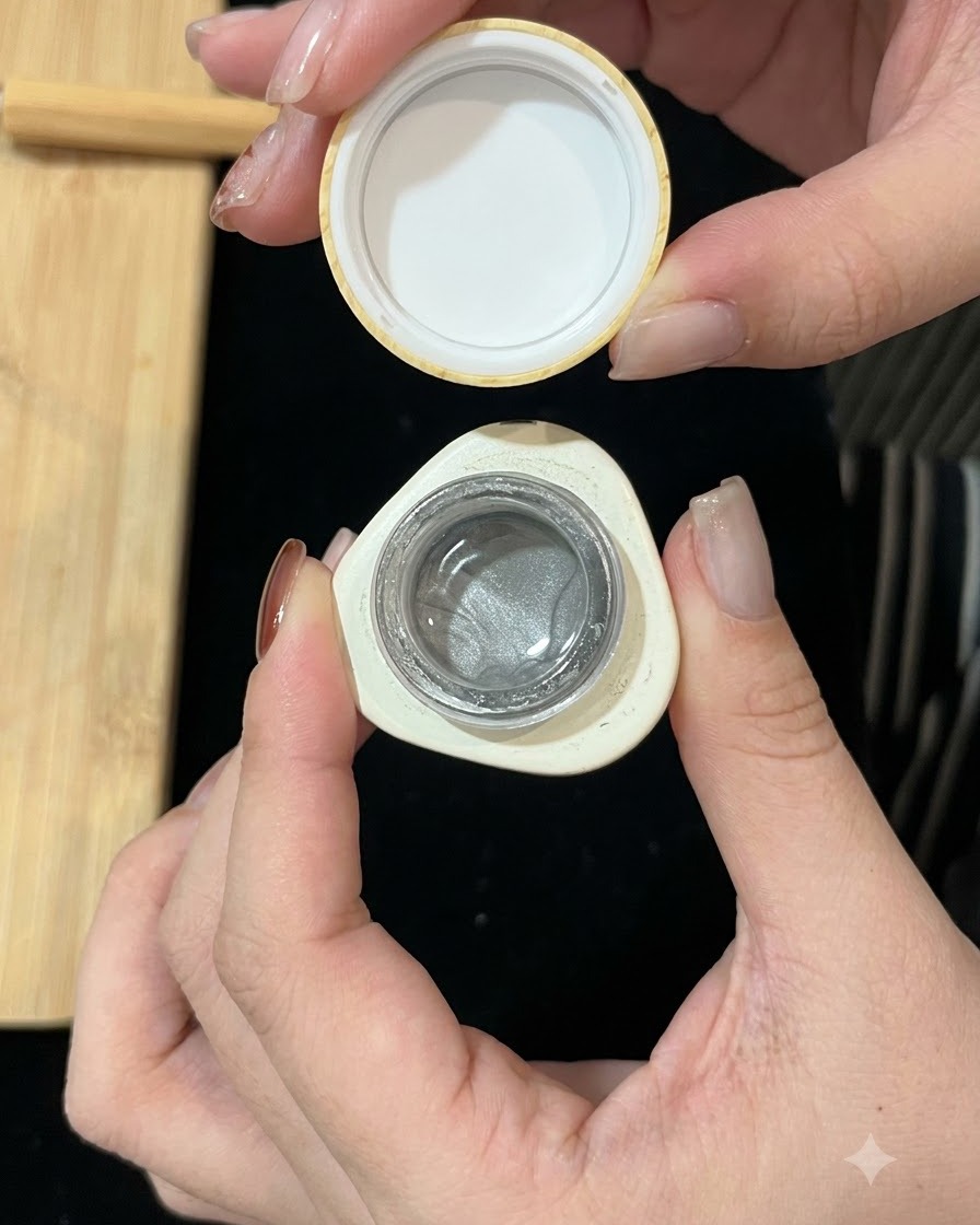 A small container of silver magnetic cat-eye gel being held open, showing the shimmery formula inside.