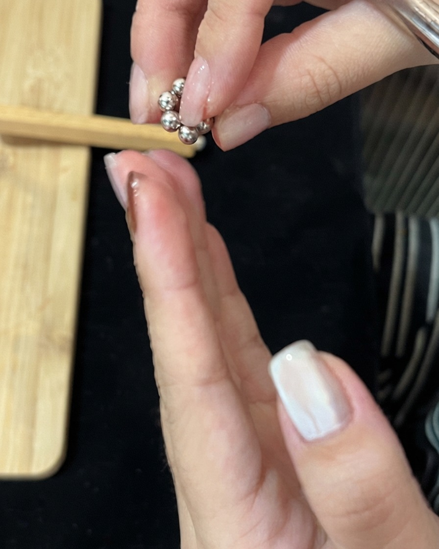 Fingers holding a small circular cluster of metallic magnetic bead balls above a hand.