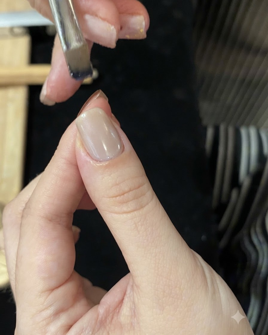 A brush loaded with blue glass gel held above a nail tip to create an ombre gradient.