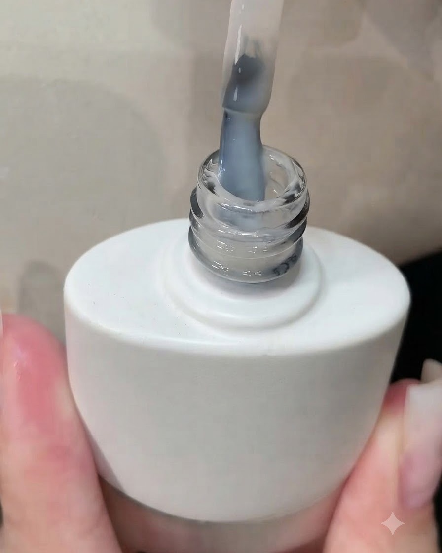A brush lifting out of a white gel polish bottle with a milky white coating visible on the bristles.