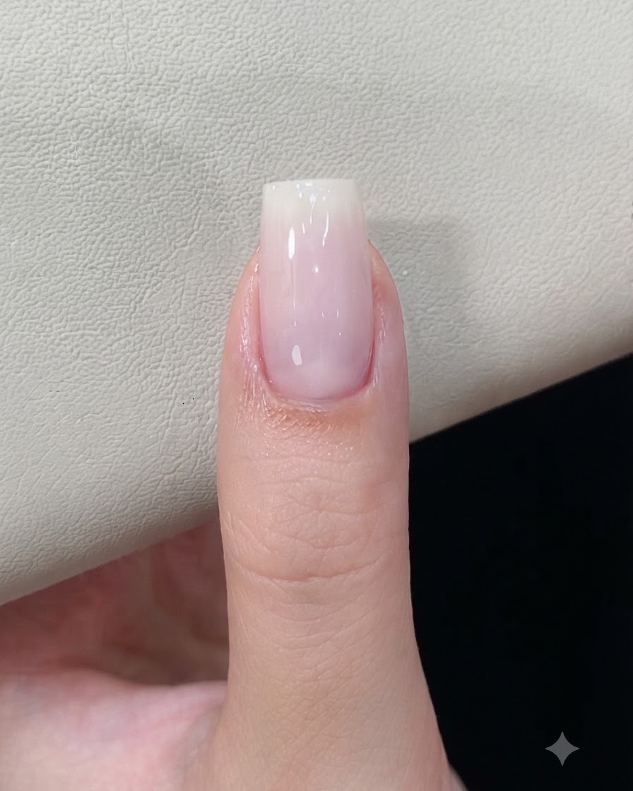 A fingernail with a cured milky white gel base resting under a nail lamp.