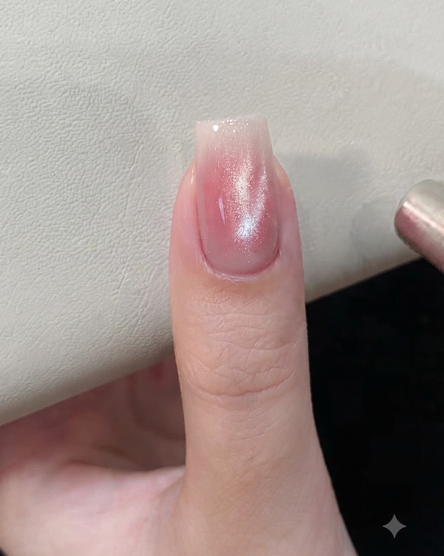A magnetic tool held near a pink and silver cat-eye gel nail to shape the magnetic particles.