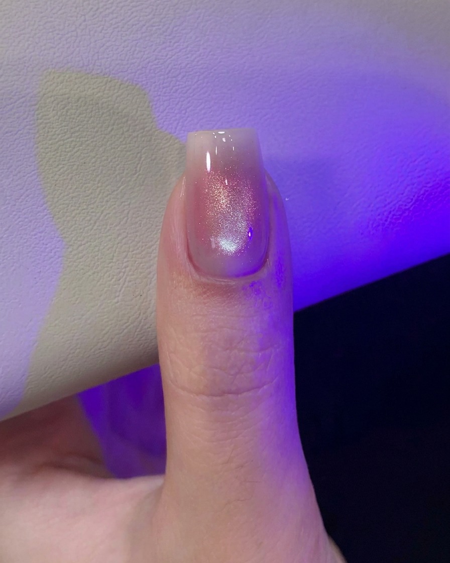 A thumb under purple UV/LED lamp light curing the freshly magnetized cat-eye nail design.