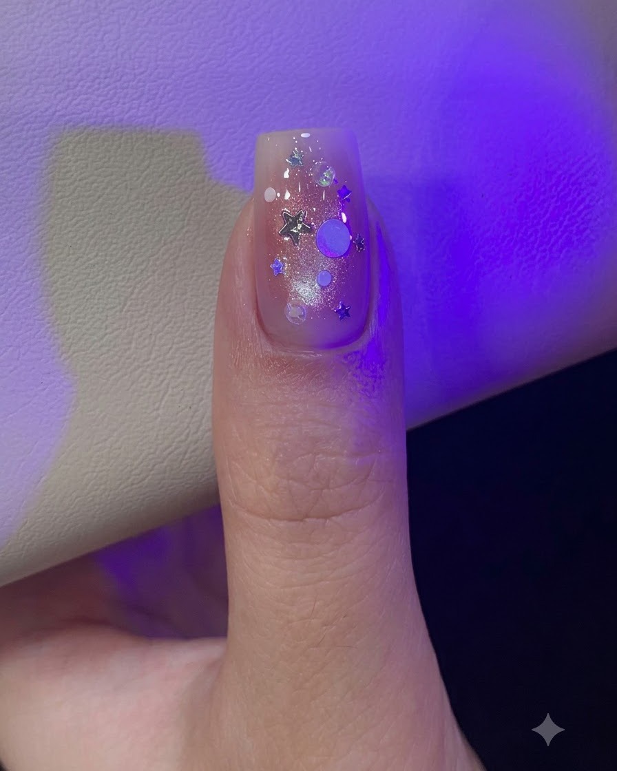 A thumb under lamp light decorated with scattered silver star and round iridescent glitter sequins.