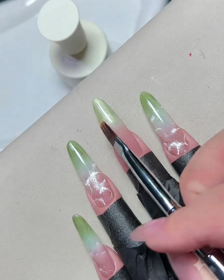 A close-up of a fine brush feathering the edge of green gel polish to create a seamless gradient blend.