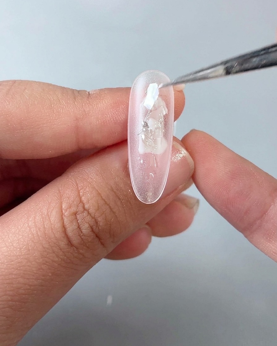 A brush tip placing small iridescent shell fragments onto the wet gel surface of a nail.
