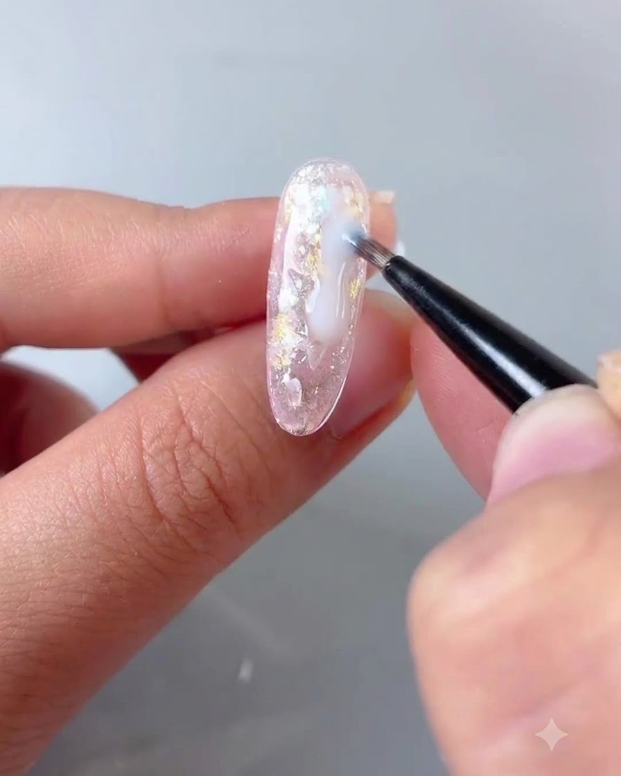 A fine brush applying a drop of milky white flowing gel into the gaps of a textured nail design.