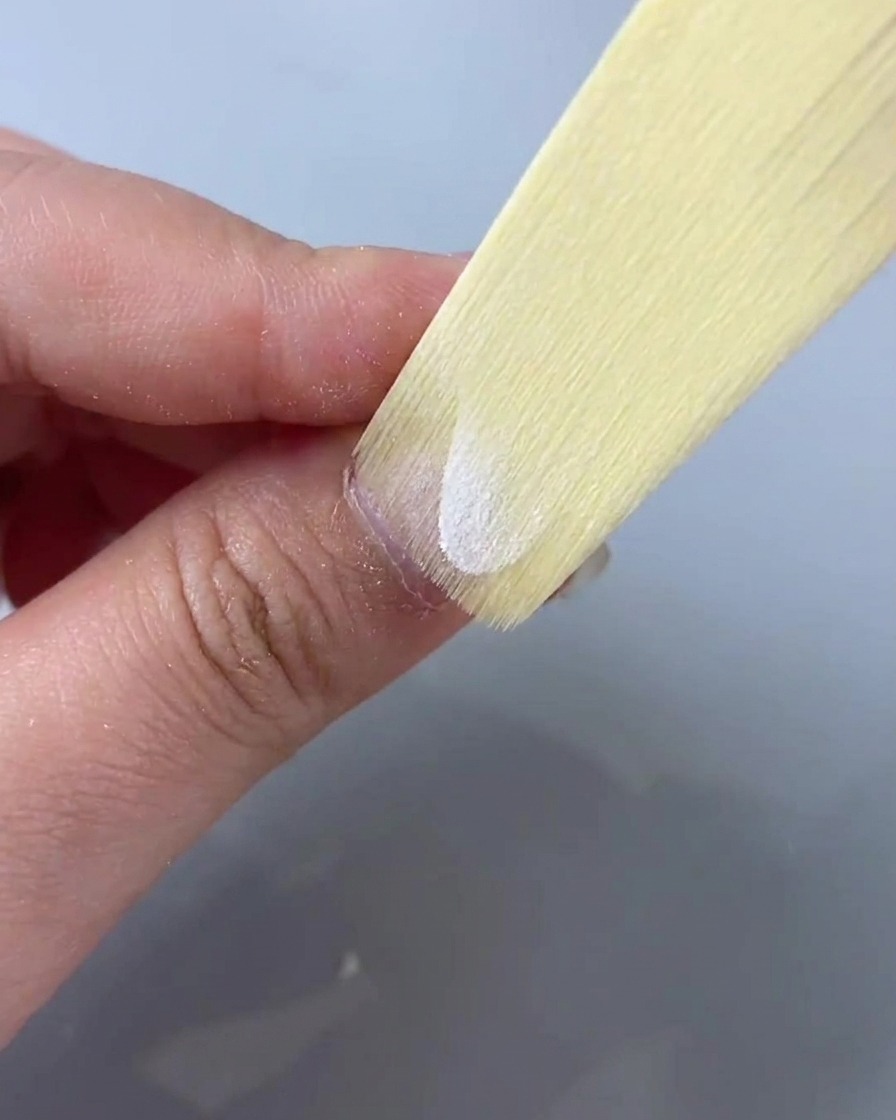 A cleansing wipe or brush sweeping across the surface of a prepped nail to remove filing dust.