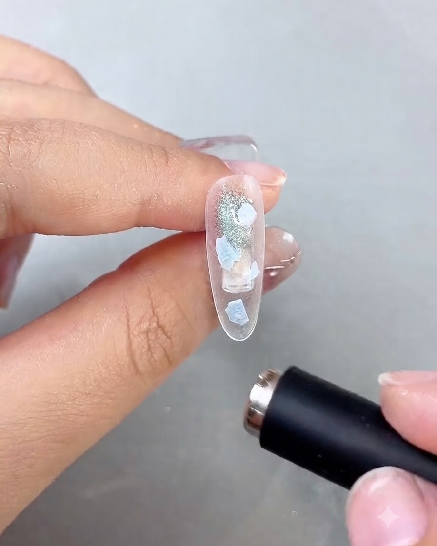 A mini black curing light held closely over a decorated nail to flash-cure the layer.