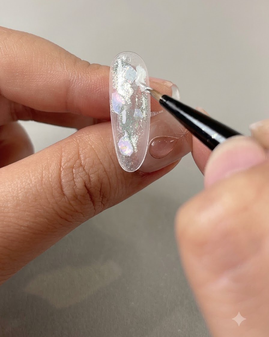 A fine brush applying pearl gel into the gaps between shell pieces on a nail.