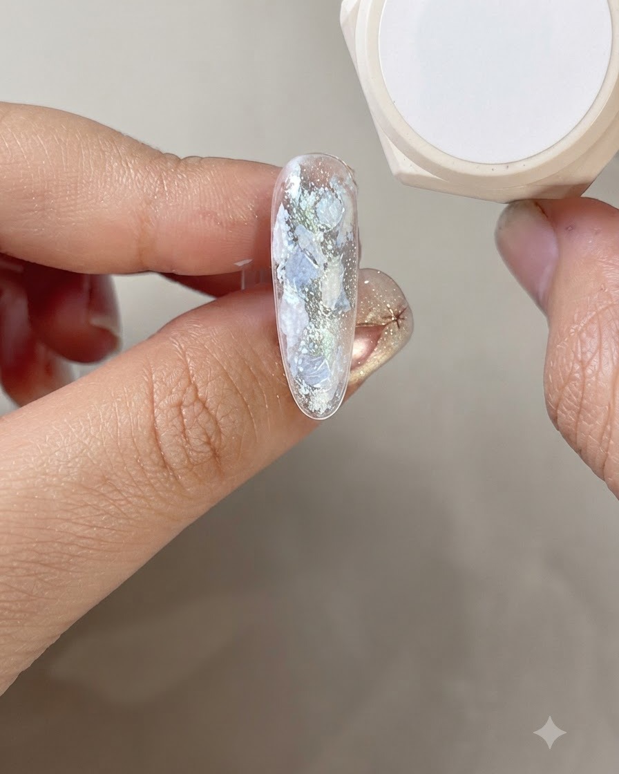 A hand positioned under a curing lamp with the nail showing cured pearl gel details.