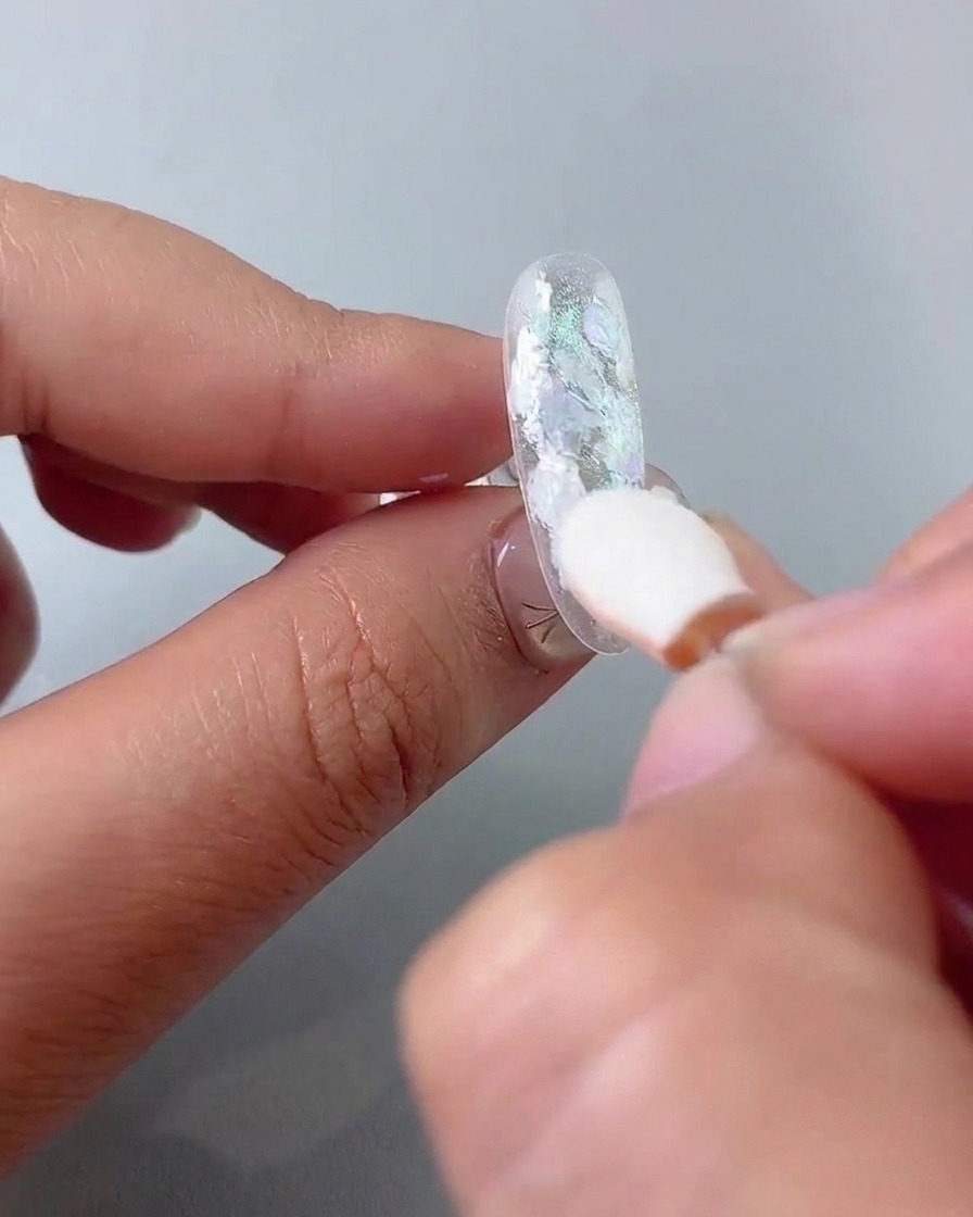 A sponge eyeshadow applicator rubbing chrome powder onto the nail surface.