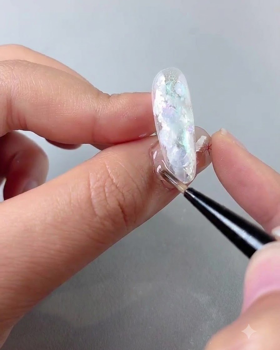A fine detail brush blending white gel dots on a nail to form a smooth blooming pattern.