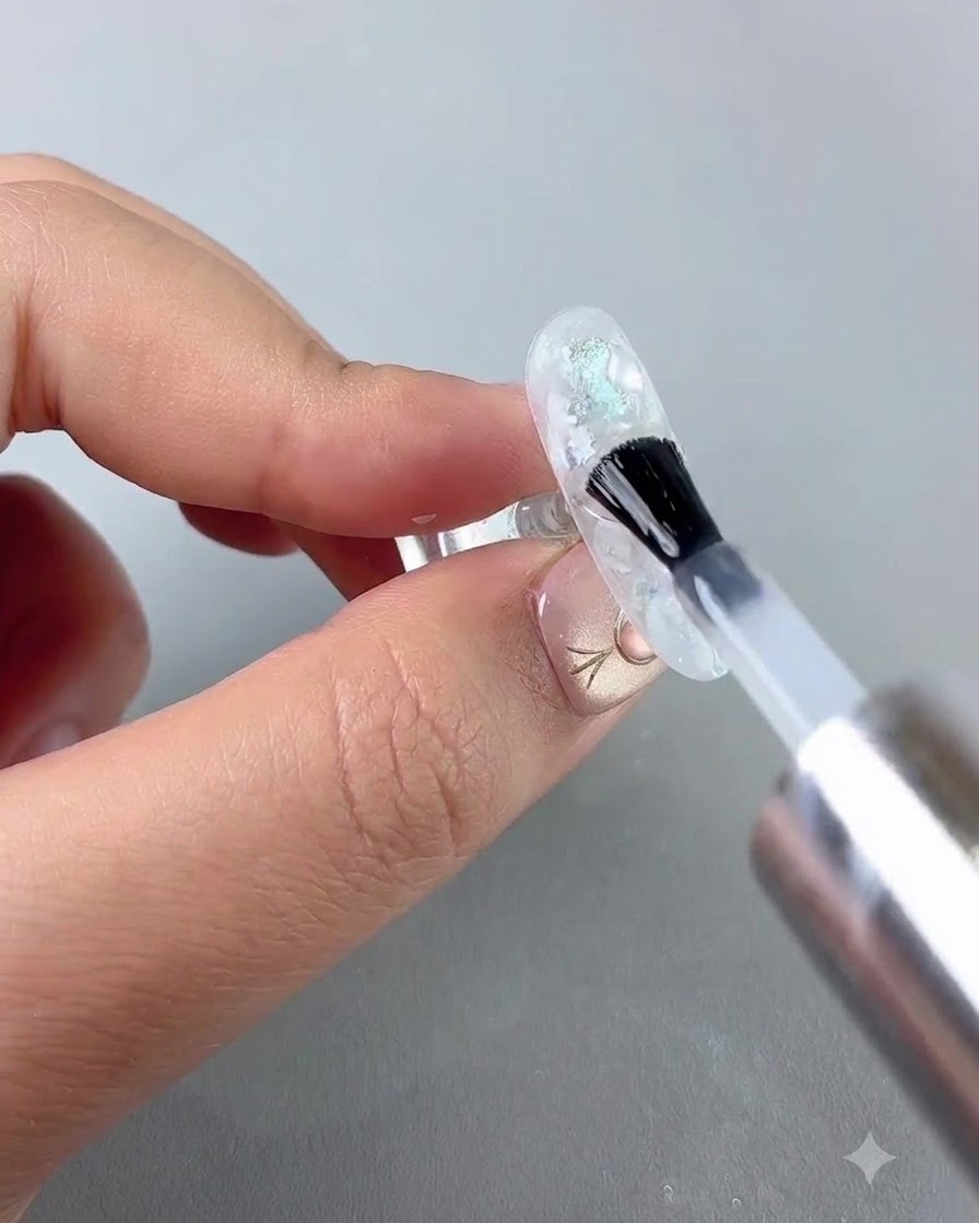 A brush applying a clear coat of soft reinforcing gel over an elaborate nail art design.