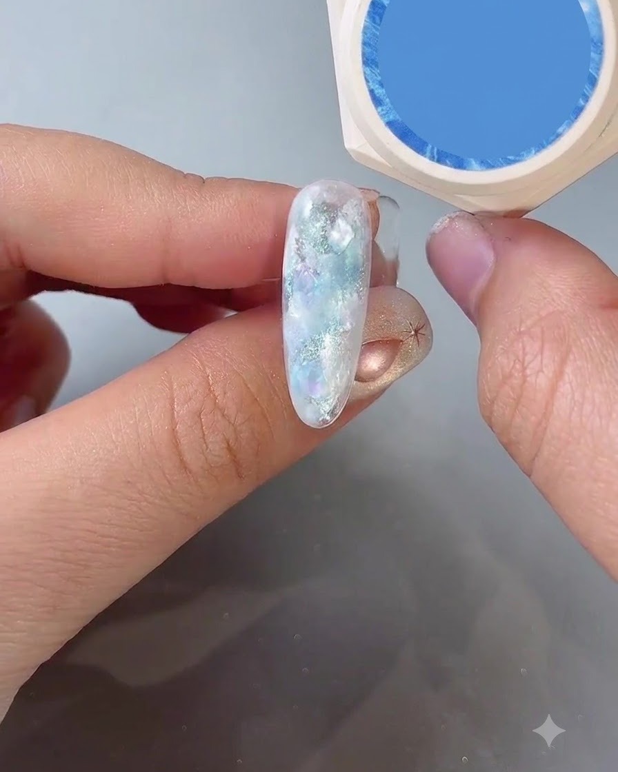 A hand holding a blue gel color bottle next to a finished nail design.