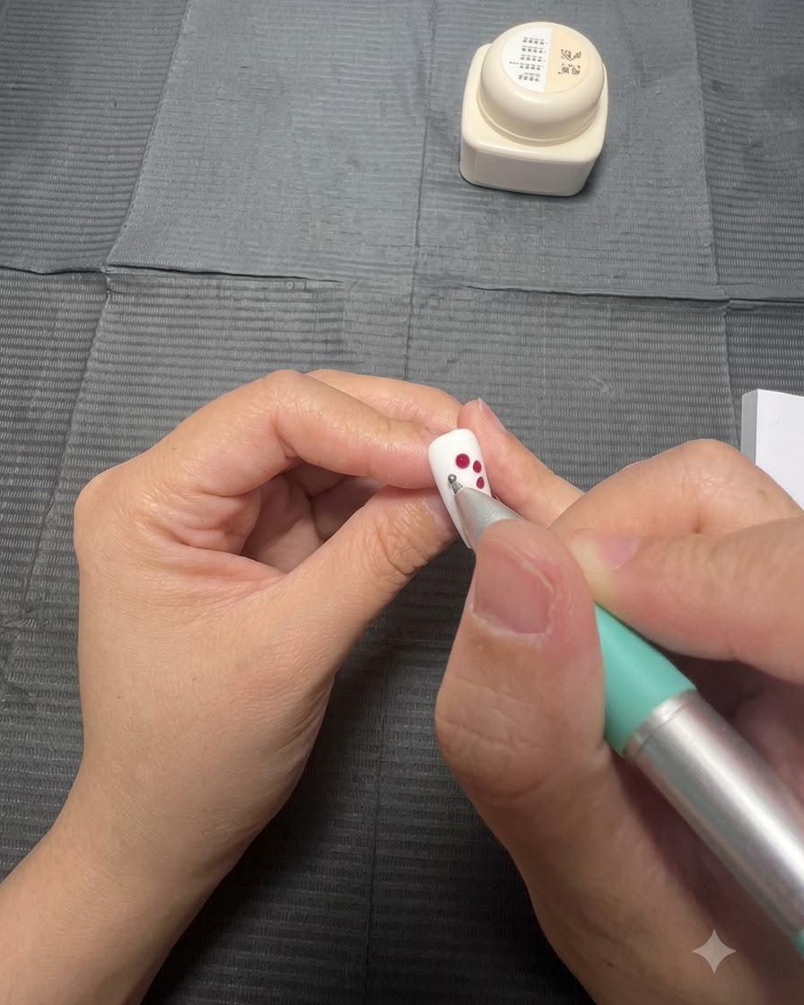 A white nail with blooming red gel dots expanding into petal shapes.
