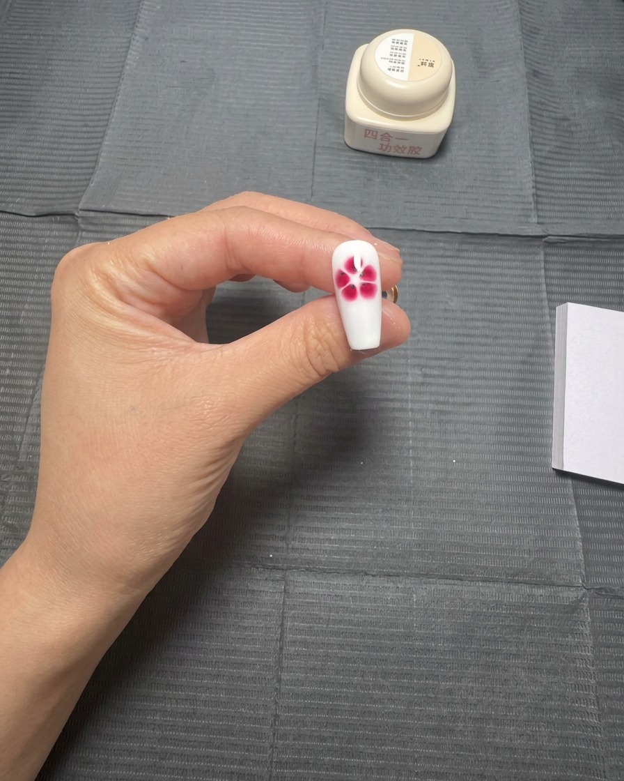 A white nail tip showing a red five-petal flower that has beautifully bloomed with a watercolor effect.