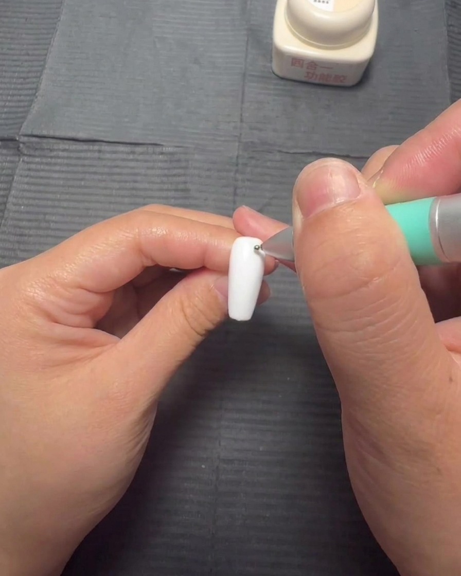 A bottle brush applying a thin layer of clear blooming gel onto a white nail.