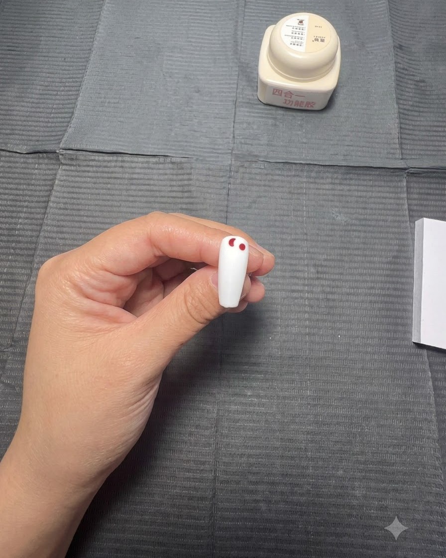 A hand using a dotting pen to place a decreasing line of red dots on a white nail.