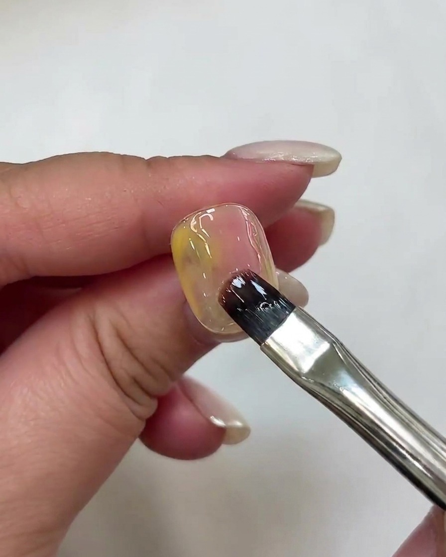A nail brush applying a deeper shade of pink gel onto the nail surface.