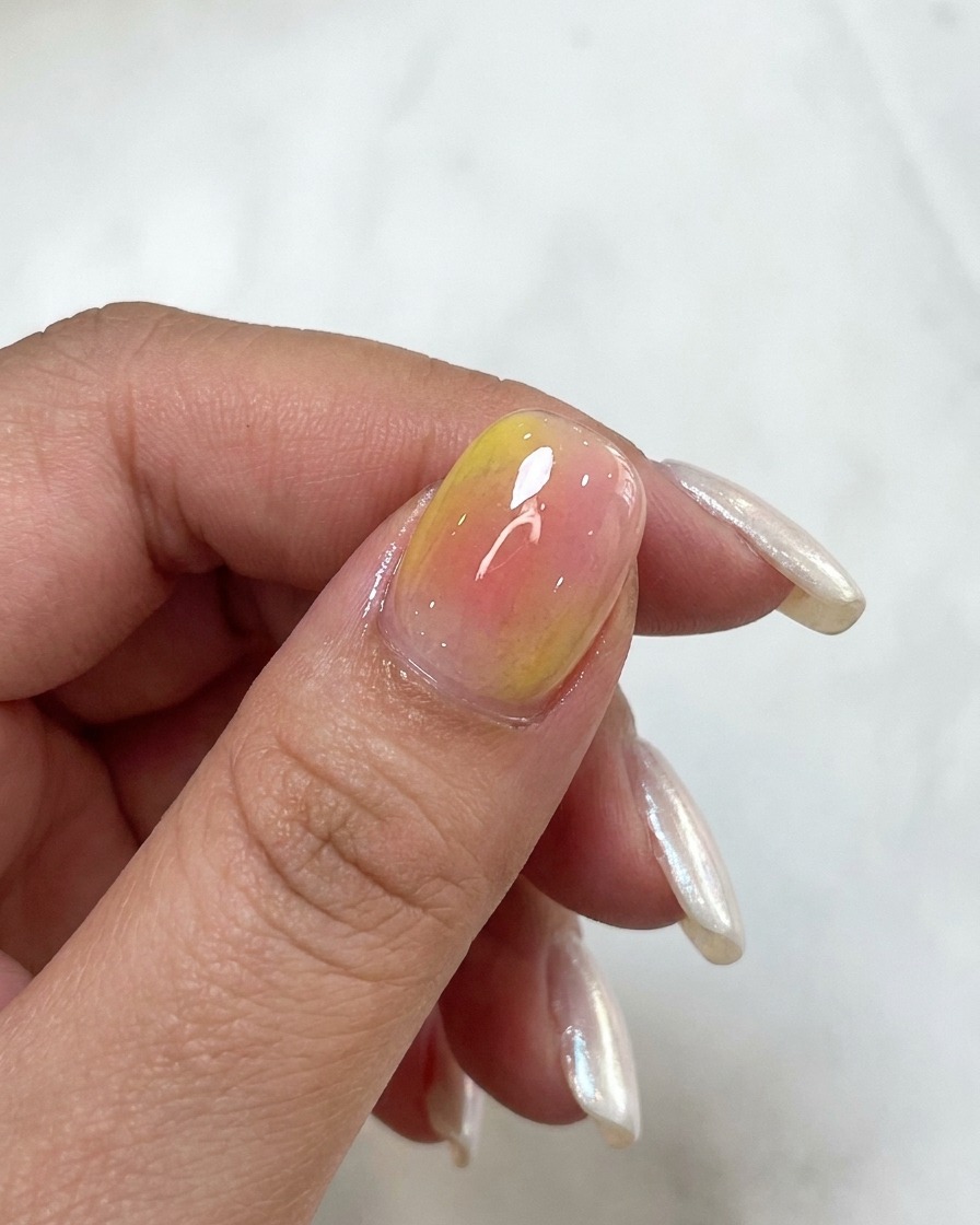 A close-up view of a nail showing layered pink and yellow watercolor tones.