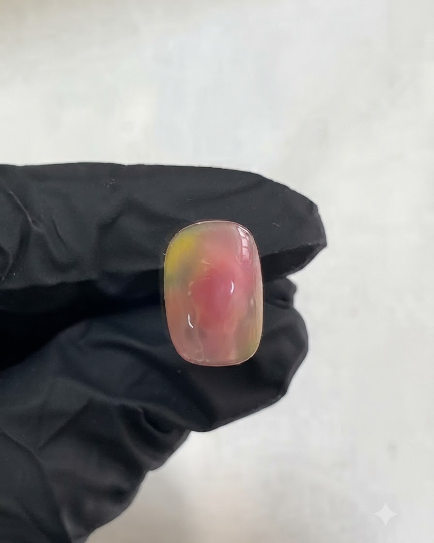 A gloved hand holding a nail showcasing the cured pink and yellow watercolor gradient design.