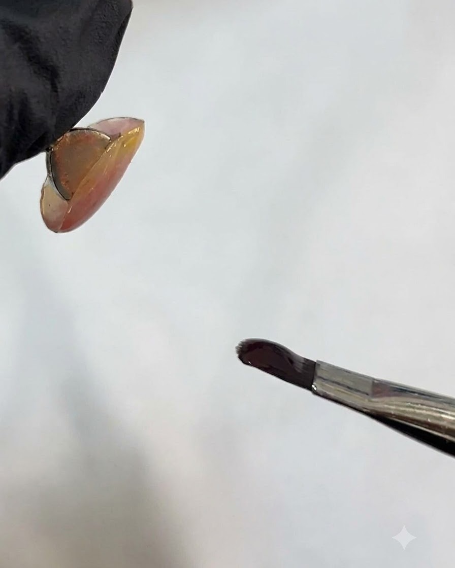 A nail brush holding dark gel near a nail surface.